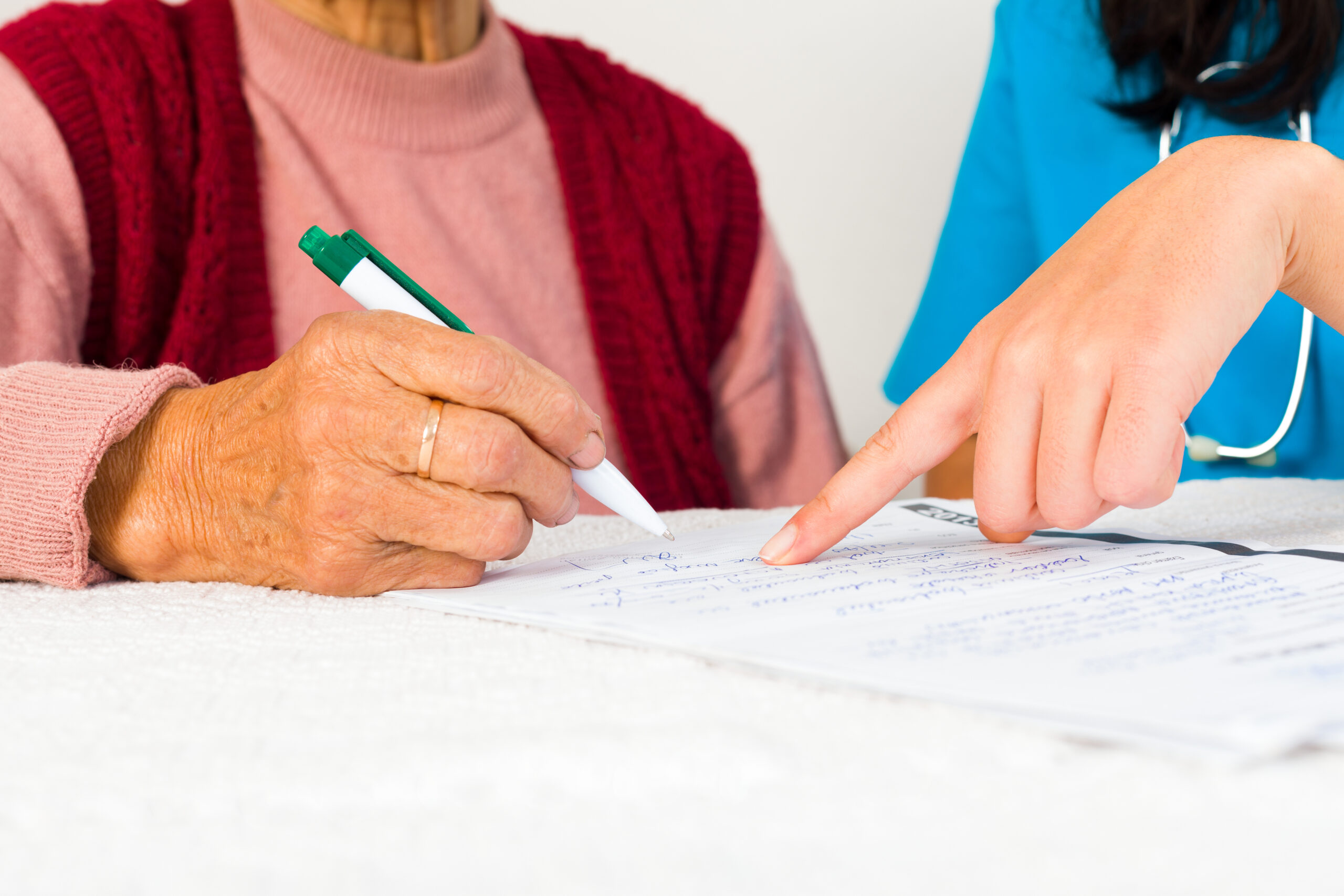 Nurse helping elderly sign a piece of paper.