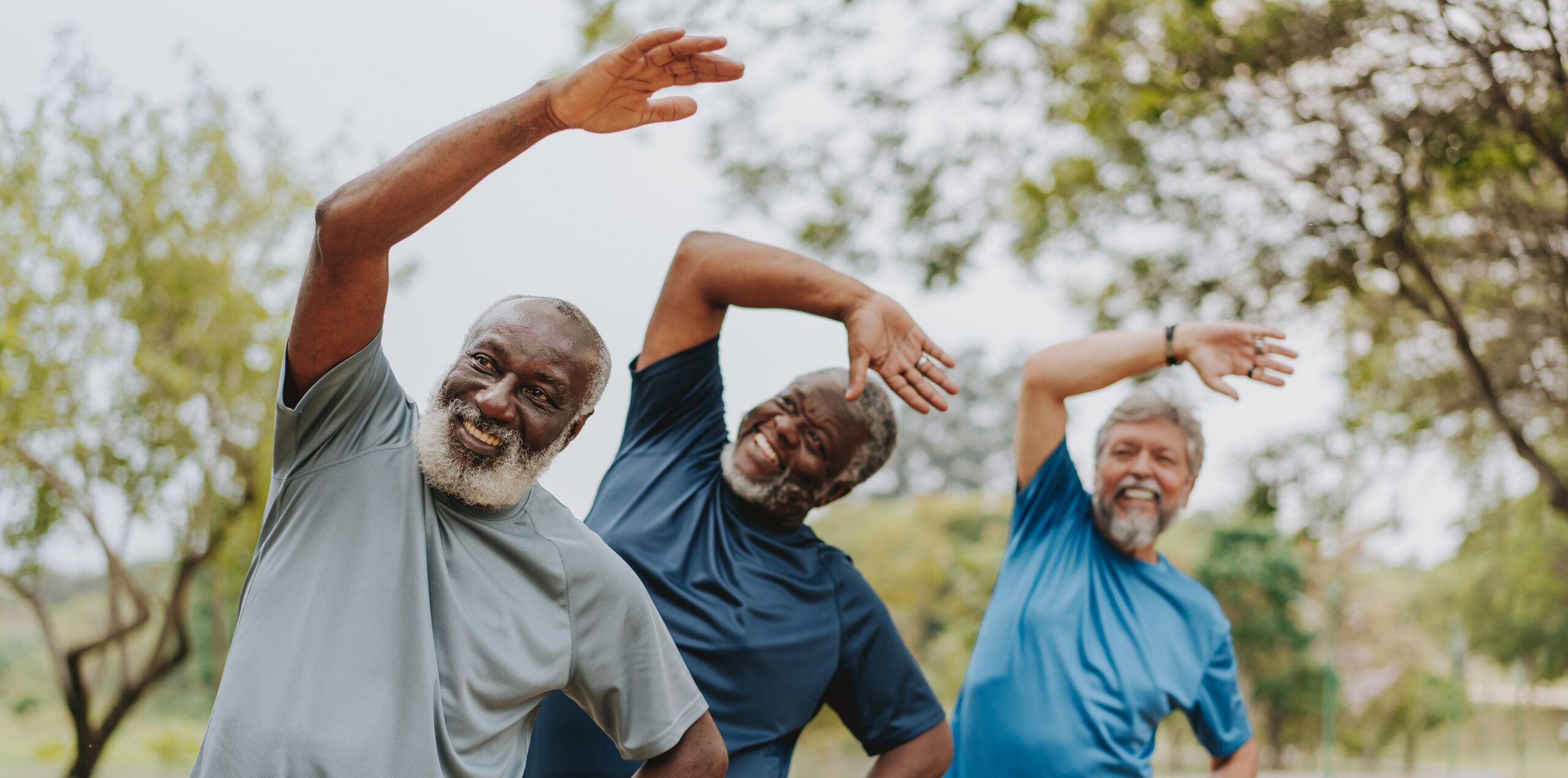 Three men smiling and doing side stretches outdoors.