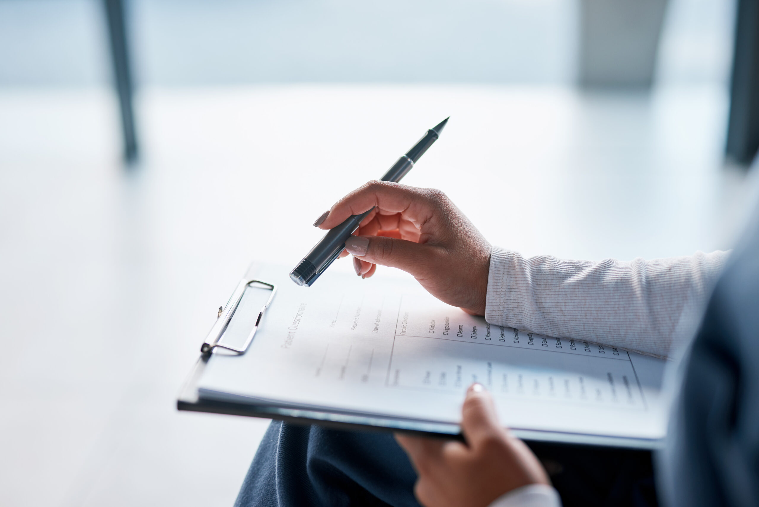 Close-up of a person's hands holding a clipboard with a "Patient Questionnaire" form, pen poised above a list of chronic condition checkboxes.