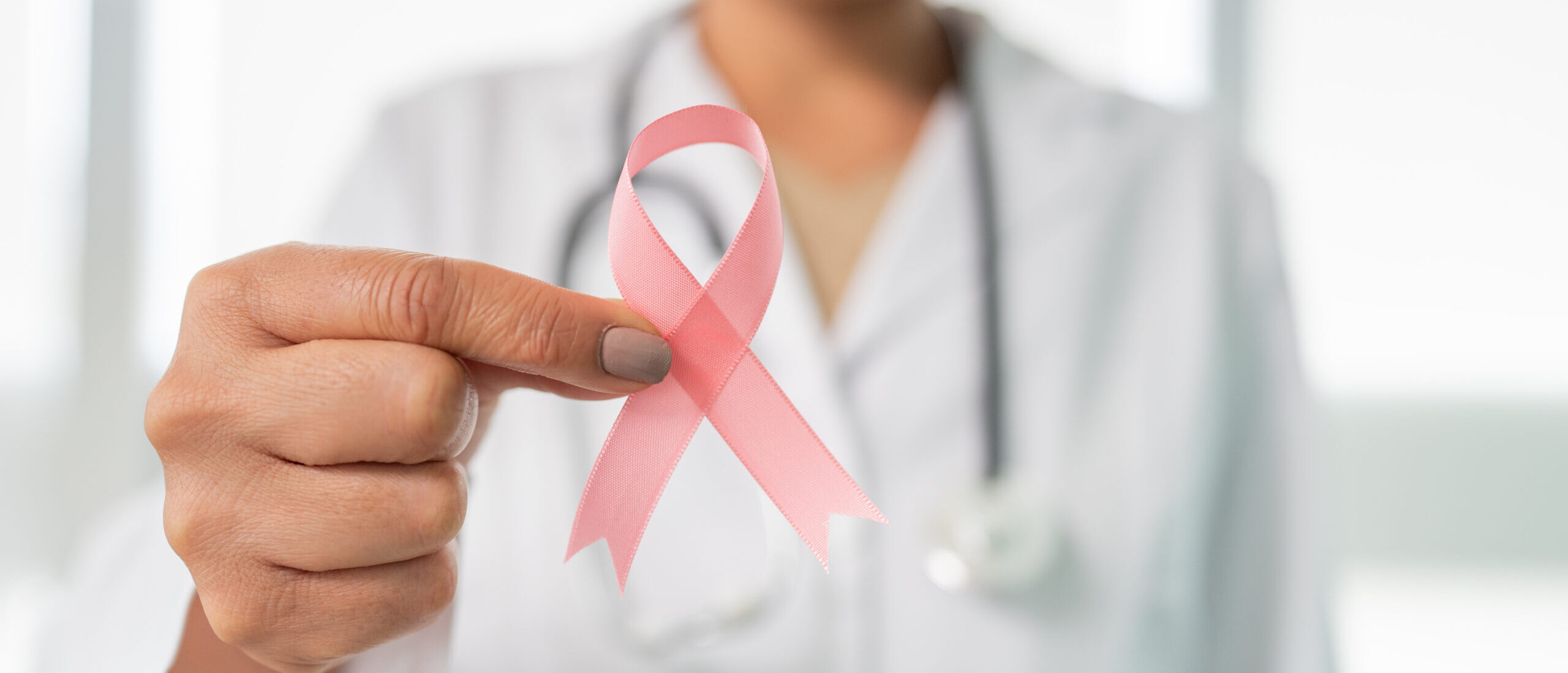 Doctor in white coat holding pink ribbon for Breast Cancer Awareness Month.