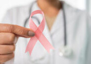 Doctor in white coat holding pink ribbon for Breast Cancer Awareness Month.