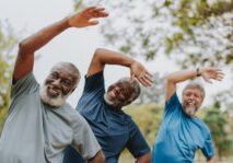 Three men smiling and doing side stretches outdoors.