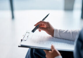 Close-up of a person's hands holding a clipboard with a "Patient Questionnaire" form, pen poised above a list of chronic condition checkboxes.